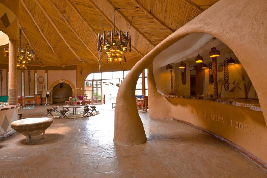 O balcão de terra esculpida da recepção, gravado com o nome do Amboseli Sopa Lodge, sob um teto de junco