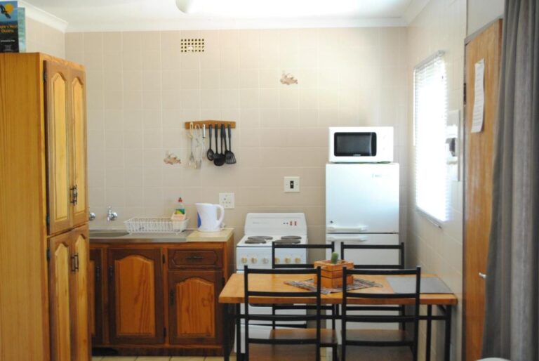 Uma cozinha equipada com cooktop elétrico, geladeira, micro-ondas e chaleira, e uma mesa para quatro