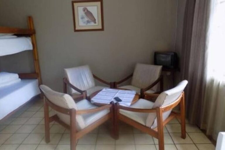 Quatro poltronas com almofadas brancas em volta de uma mesa de centro, ao lado de um beliche, sob um quadro de coruja