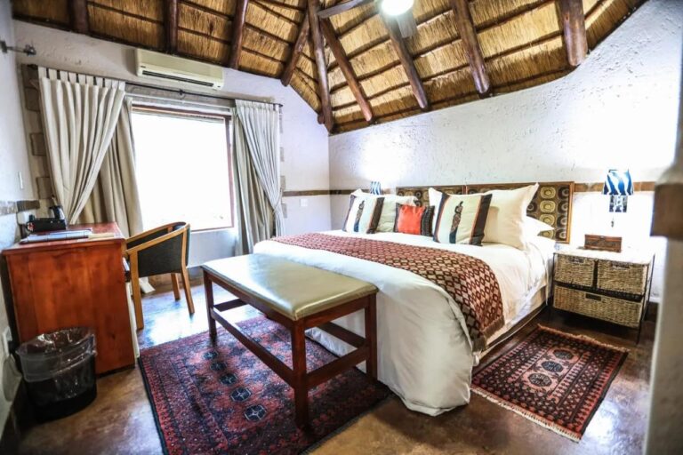 Um quarto sob a palha, com ar-condicionado, escrivaninha de madeira e um banco aos pés da cama