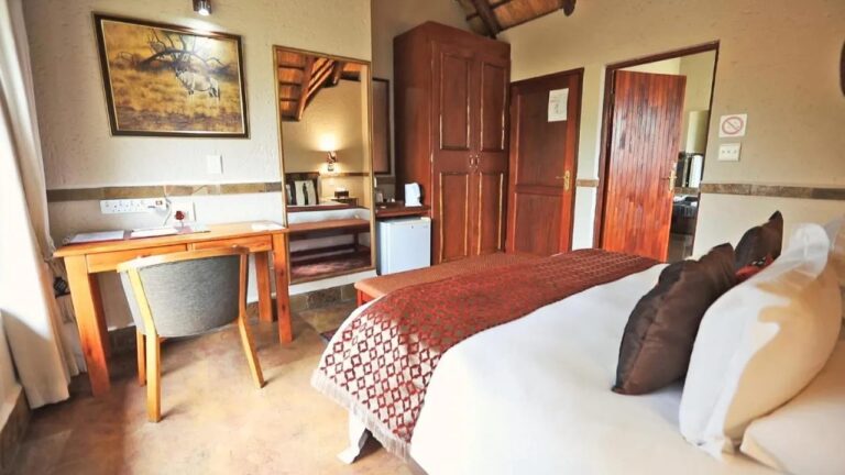 Um quarto com escrivaninha, guarda-roupa de madeira, uma pequena geladeira e o quadro de um órix na parede