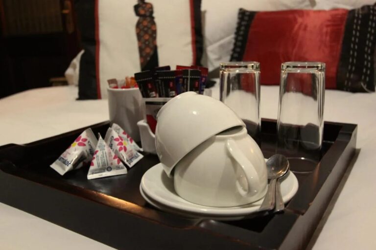 Uma bandeja com xícaras, copos e sachês de chá e café, sobre uma cama