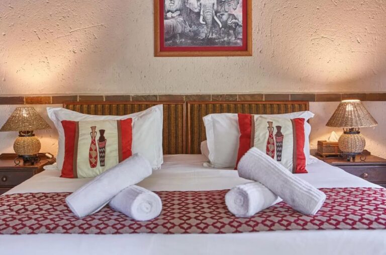 Uma cama de casal com toalhas enroladas, sob uma imagem em preto e branco de leão, elefante, rinoceronte e búfalo