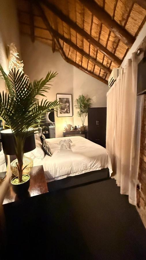 Um quarto sob a palha, com cama de casal, guarda-roupa escuro e cortinas de voil diante da janela