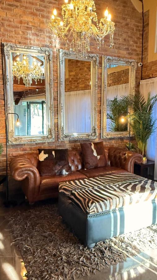 Um sofá Chesterfield de couro e um pufe zebrado sob um lustre de cristal, diante de três grandes espelhos e de uma parede de tijolos