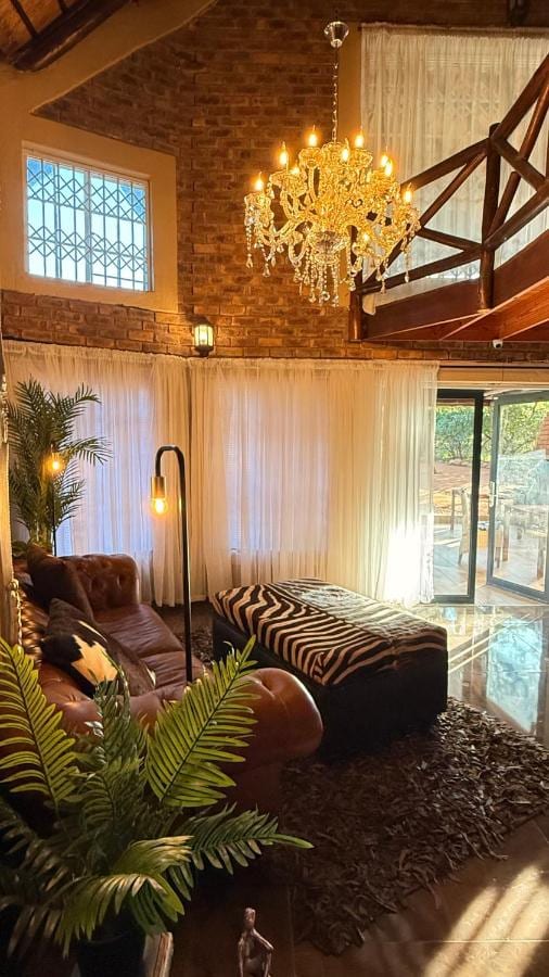 A sala de estar sob uma estrutura de telhado alta, com lustre, sofá de couro, pufe zebrado e mezanino de madeira