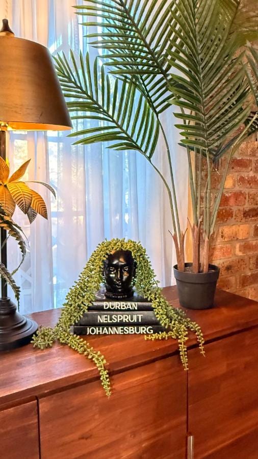 Um busto preto sobre três livros, rodeado por uma planta pendente, em um móvel de madeira perto de uma palmeira