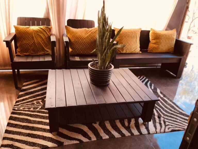 Uma sala de estar com assentos de madeira escura, almofadas amarelo-mostarda e uma mesa de centro sobre um tapete zebrado