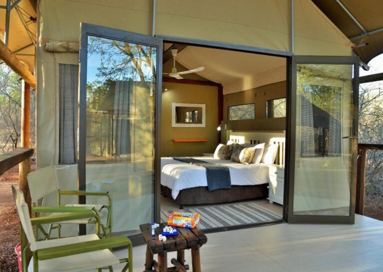 Uma tenda vista do terraço, com as portas de vidro abertas para a cama e poltronas verdes na frente