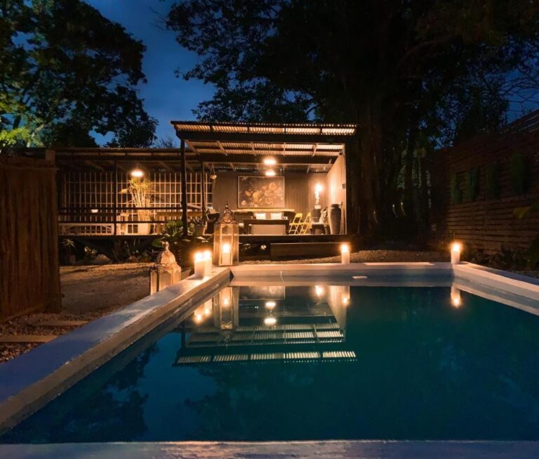 A piscina do Lush ao anoitecer, iluminada por velas, diante de um terraço coberto com telhado de zinco