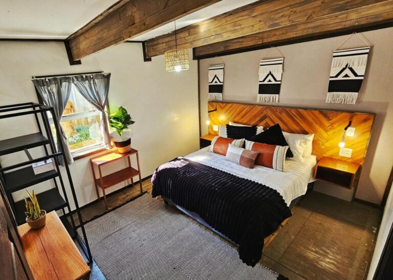 Um quarto do The Elements com cama de casal, cabeceira de madeira em espinha de peixe e três tapeçarias em preto e branco, sob vigas aparentes