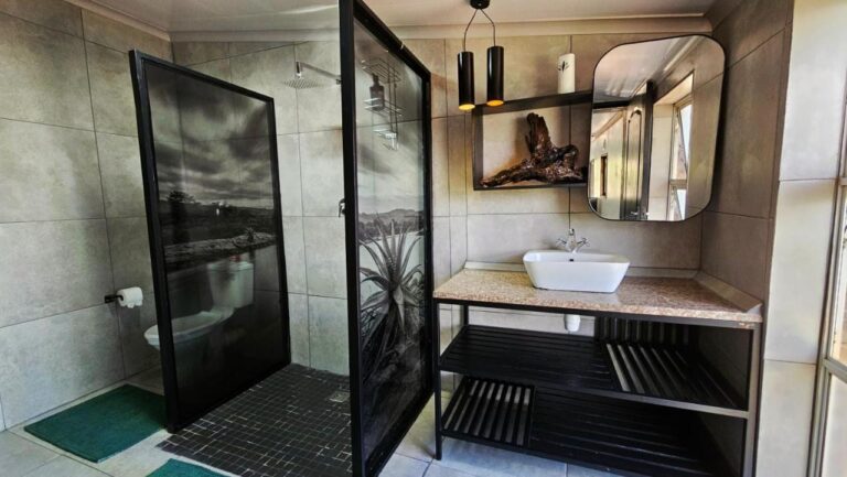Um banheiro com chuveiro atrás de painéis de vidro decorados com fotos em preto e branco, e uma cuba de apoio sobre um móvel preto