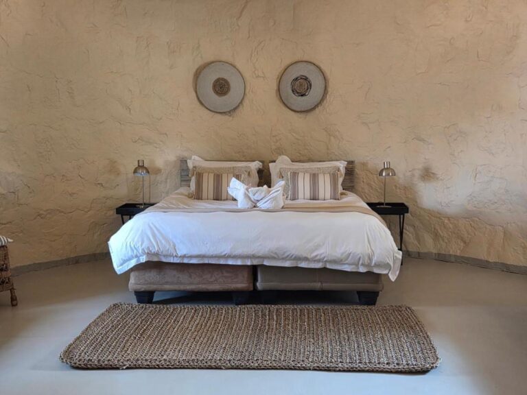 Uma cama de casal sob dois discos decorativos, entre dois abajures, com um tapete trançado