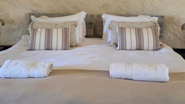 Almofadas listradas e toalhas dobradas sobre uma cama de casal branca