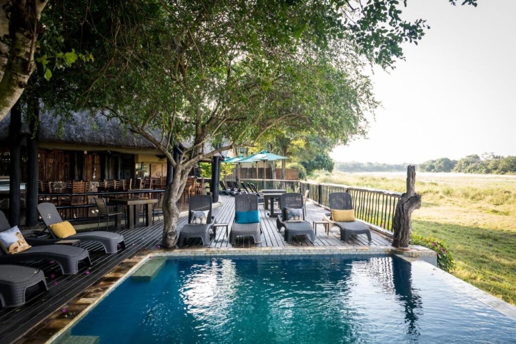 A piscina do Umkumbe Safari Lodge e o terraço de madeira, acima da margem gramada do rio