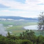 O fundo verde da cratera visto da borda, com o lago Magadi e nuvens presas às encostas