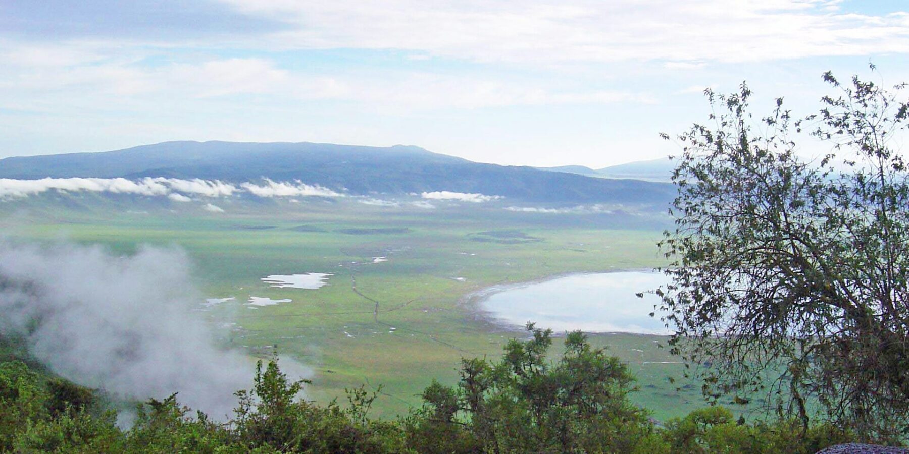 O fundo verde da cratera visto da borda, com o lago Magadi e nuvens presas às encostas