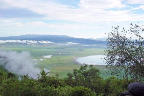 O fundo verde da cratera visto da borda, com o lago Magadi e nuvens presas às encostas